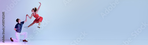 Photography Beautiful young couple, man and woman in stylish clothes dancing retro style dances over gradient blue purple studio background