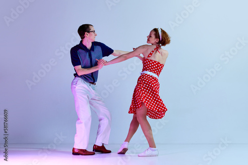 Billede på lærred Beautiful young couple, man and woman in stylish costumes dancing retro dances against gradient blue purple studio background