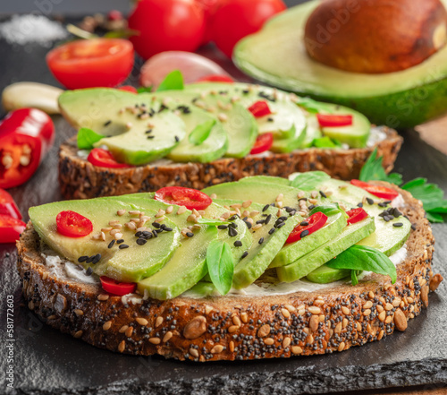 Avocado toasts - bread with avocado slices, pieces of red pepper and sesame on black stone board.