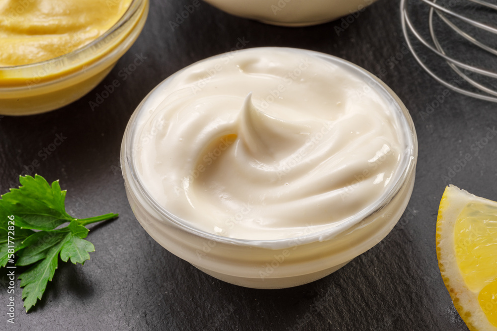 Glass bowl of homemade mayonnaise on black stone slate serving plate close-up. Glass bowl of homemade mayonnaise on black stone slate serving plate close-up.
