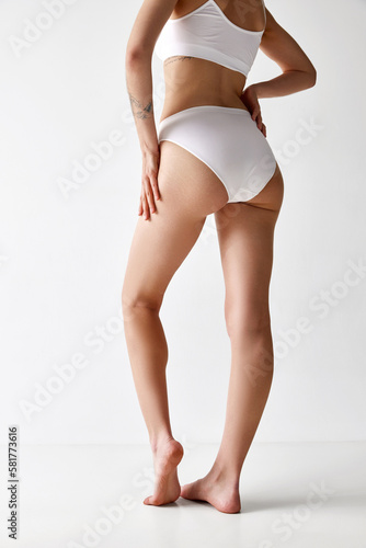 Cropped image of slender young woman with sportive body shape in cotton inner wear posing over white background. Back view