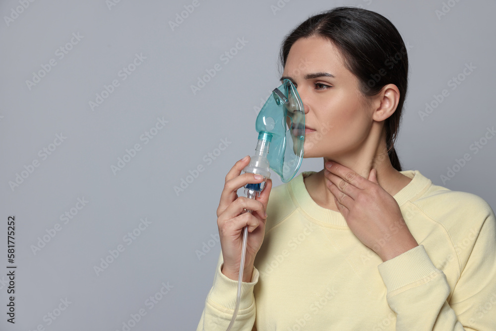 Sick young woman using nebulizer on grey background, space for text Sick young woman using nebulizer on grey background, space for text