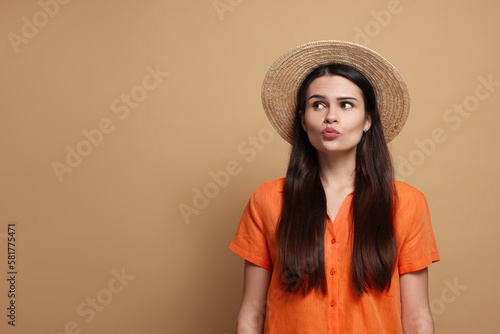 Beautiful young woman in straw hat giving kiss on beige background. Space for text