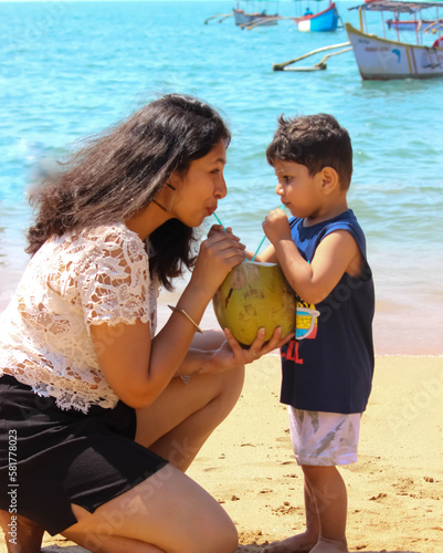 A mother and son drinking coconut water from a single coconut on a lovely butterfly Iceland at Palolem beach, sount Goa, India photo