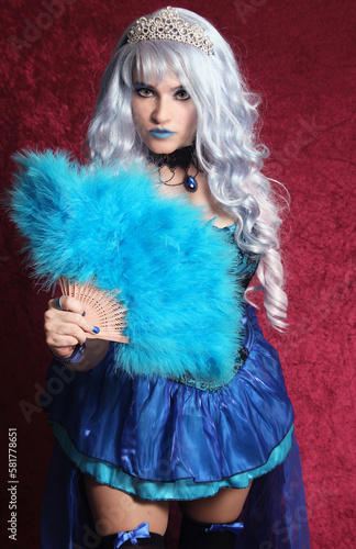 Woman With Blue Hair and Blue Corset Dress Holding Blue Fan on Red Velvet Background
