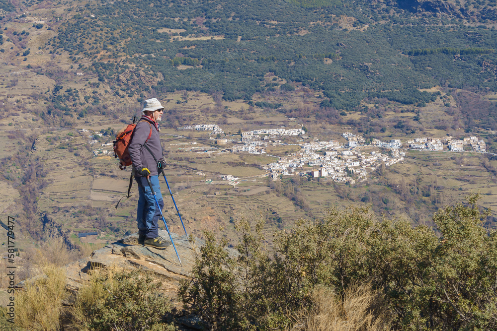 A man standing in the mountains, with a picturesque village in the distance.