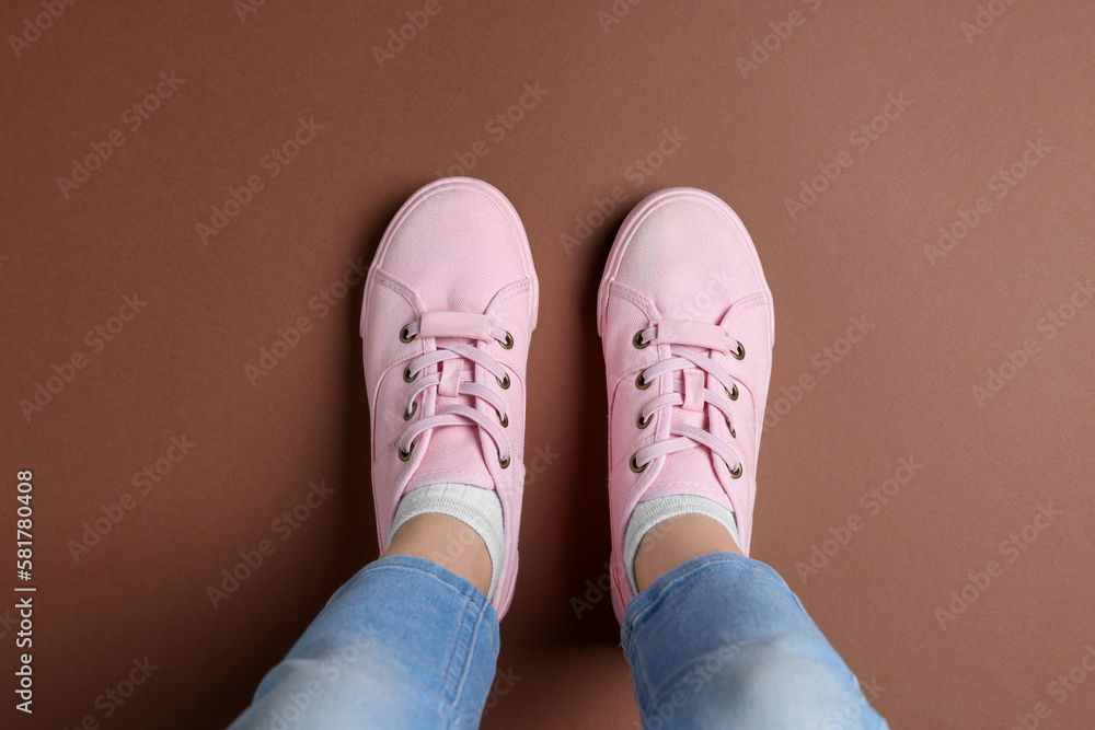Woman in stylish sneakers standing on brown background, top view Woman in stylish sneakers standing on brown background, top view