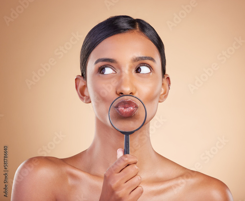 Mouth, lips or woman with magnifying glass in studio on beige background searching for facial beauty. Face, headshot or young Indian girl looking for luxury self care cosmetics, lipstick or makeup