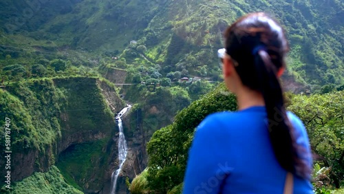 Woman from behind in blue sweater looking at Devil's Caudron waterfall. Ecuador. Static view photo