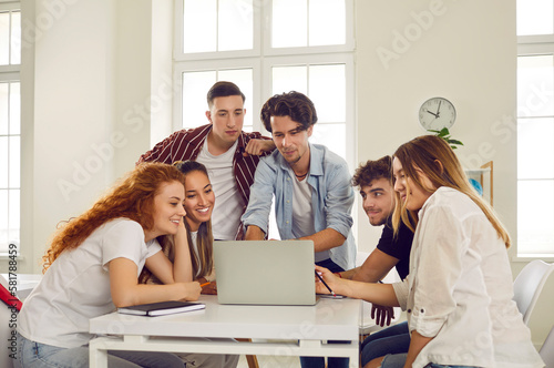 Company of smart young business college or university students cooperate, gather in campus library, use laptop computer, study sales data, do marketing research, prepare group presentation for class