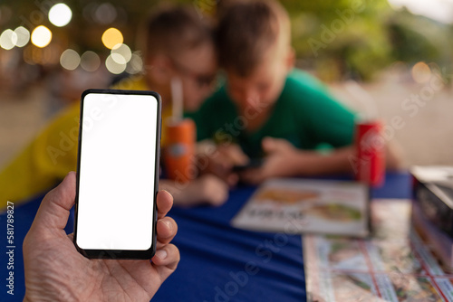 smart phone in hand on the background of children in beach cafe