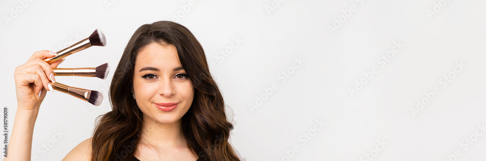 Beautiful brunette woman holding brushes near the face on the grey background with copy space. Beautiful brunette woman holding brushes near the face on the grey background with copy space.