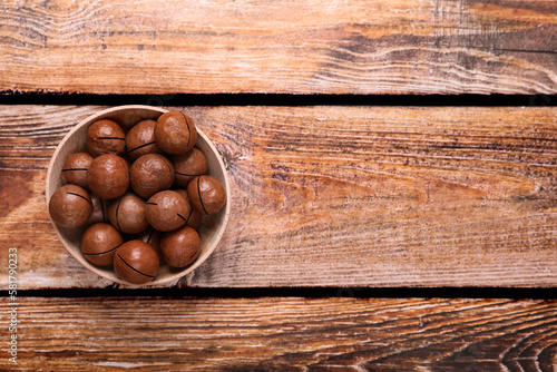 Delicious organic Macadamia nuts in bowl on wooden table, top view. Space for text