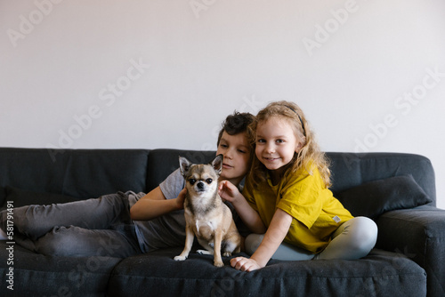 2 children sitting on the couch petting a small chihuahua dog, portrait, close up, lifestyle