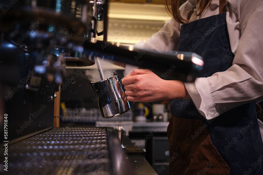 Close up of a barista preparing milk for coffee on a espresso machine in coffee shop.