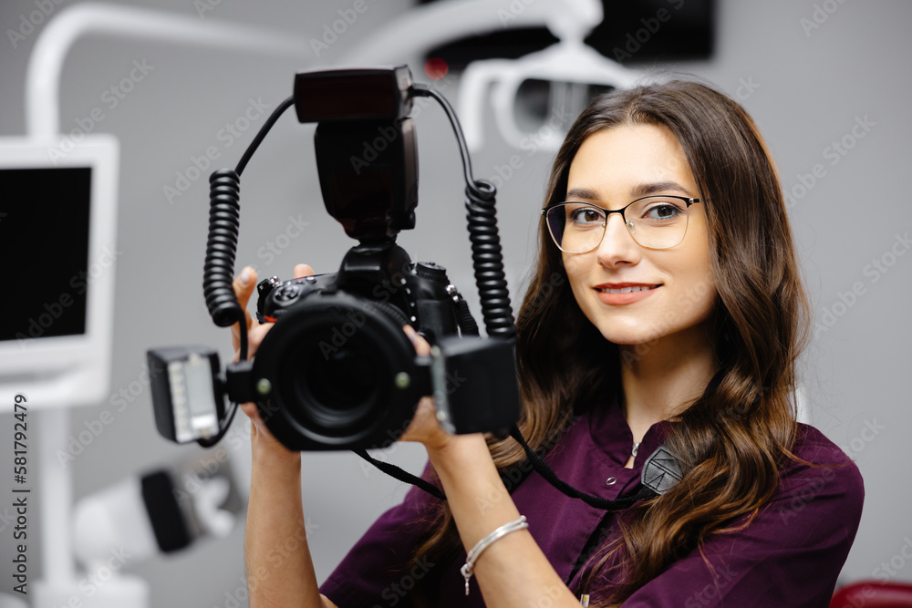 Portrait of female dentist holding photo camera in hands, standing in dental office Portrait of female dentist holding photo camera in hands, standing in dental office