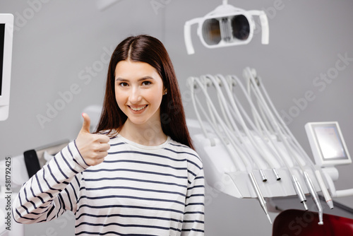 Smiling happy girl showing thumb up gesture sit at dental office chair indoor cabinet waiting stomatologist for oral procedure Healthcare caries enamel treatment.