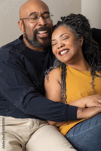 Lifestyle portrait of an attractive black middle aged couple. They are sitting on the couch and they are laughing. They are relaxing and enjoying each other's company in the living room. 