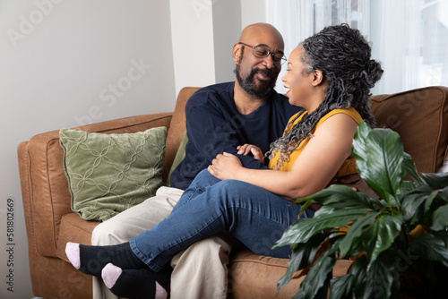 Lifestyle portrait of an attractive black middle aged couple. They are sitting on the couch and they are laughing. They are relaxing and enjoying each other's company in the living room. 