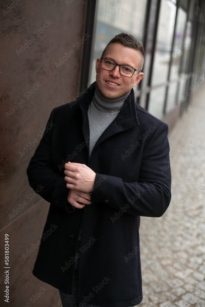 Handsome smiling man in glasses and black coat near building. Portrait of business man walking outdoors in cold day.