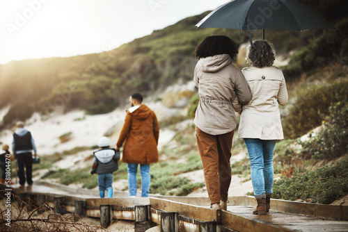 Back, nature and a family walking on a wooden path outdoor together for holiday or vacation. Love, environment and bonding with relatives taking a walk near the beach while bonding in winter