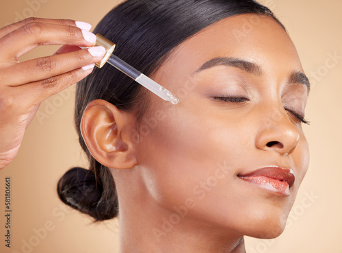 Woman, dropper and retinol on face for skincare beauty or cosmetics against studio background. Calm beautiful female model applying oil drop to skin for hydration, moisturizer or facial treatment