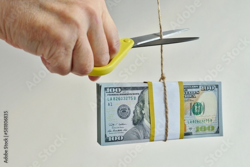 Hand with scissors cutting a rope with hanging bundle of hundred-dollar bills. The concept of solving the problem of getting rid of debts and repayment of loans,