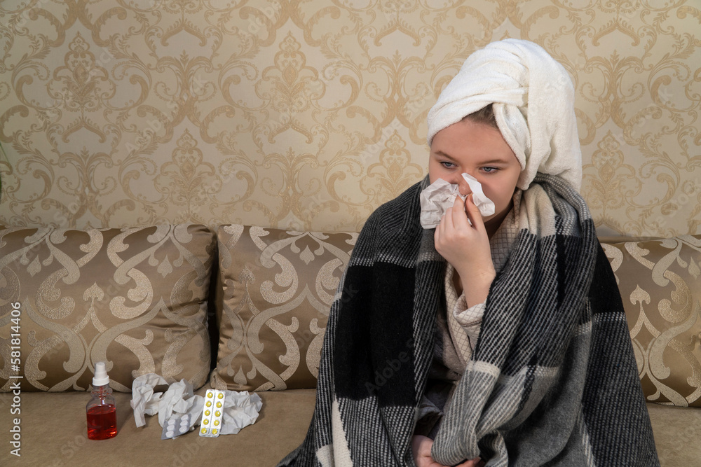 A girl with cold symptoms sits on a sofa and blows snot into a paper handkerchief. Concept of medicine, healthcare, pharmacy and home treatment A girl with cold symptoms sits on a sofa and blows snot into a paper handkerchief. Concept of medicine, healthcare, pharmacy and home treatment