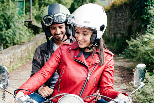 Happy couple on motorbike. Young girl and boy on motorbike happy laughing while driving on the road in safety helmet. Couple on scooters smiling as they take a trip on the parkway