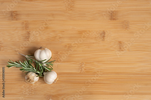 Garlic and rosemary on kitchen wooden table with copy space .