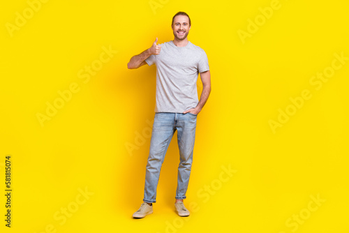 Full length photo of positive nice guy dressed light t-shirt arm in pocket showing thumb up good job isolated on yellow color background