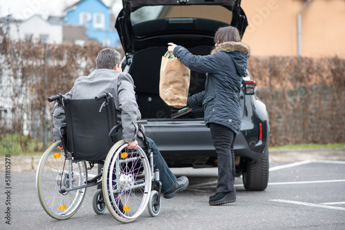 A woman helps a disabled person on a wheelchair to pack groceries into the car © Natalje Dietrich