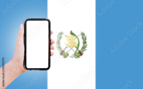 Male hand holding smartphone with blank on screen, on background of blurred flag of Guatemal. Close-up view. photo