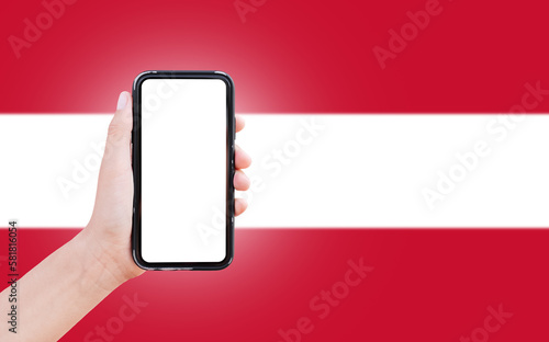 Male hand holding smartphone with blank on screen, on background of blurred flag of Austria. Close-up view.