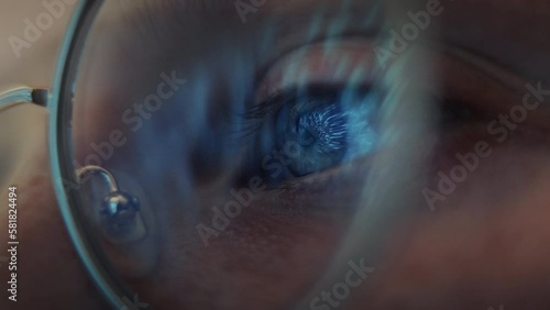 Close up view of blue eye, looking at the light movement late at night. Macro shot of the eye with lights reflections. Female with protective computer glasses.