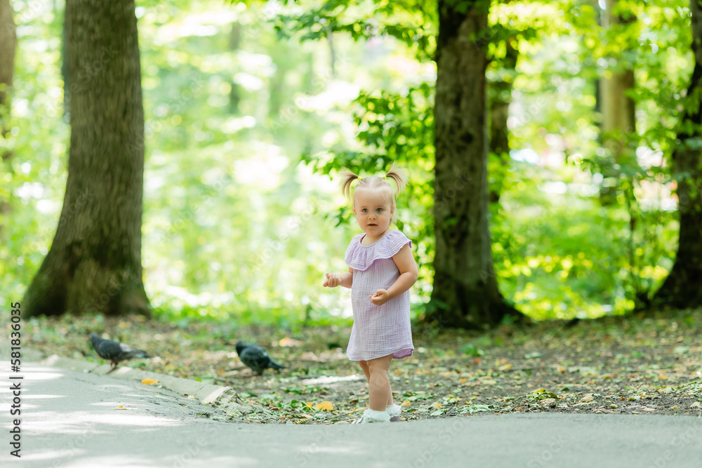 cute little girl in a purple muslin dress walks in the park in the woods in summer.Earth Day. Children Protection Day cute little girl in a purple muslin dress walks in the park in the woods in summer.Earth Day. Children Protection Day
