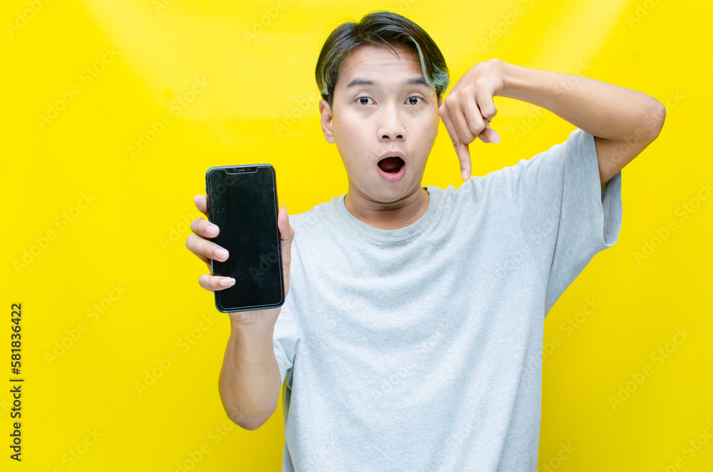 ecstatic Asian young man with peek-a-boo hair showing his phone screen isolated over yellow background. best for model advertising. ecstatic Asian young man with peek-a-boo hair showing his phone screen isolated over yellow background. best for model advertising.
