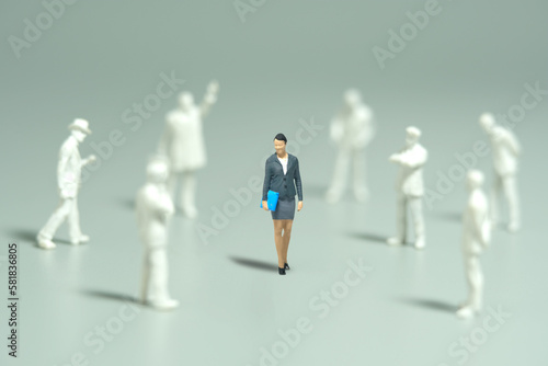 Miniature people toy figure photography. Women empowerment concept. A businesswoman standing in the middle of male people crowd shadows