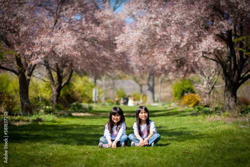 Two young asian girls sitting in large garden with sakura at full blossom in spring