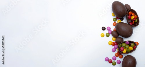 Horizontal banner with space for text. Top view. Sweets for children. Chocolate egg and multi-colored small round candies on white background. Happy Easter. Copyspace. Religious holiday celebration