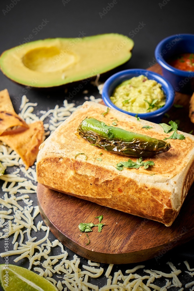 Plate of freshly-prepared chimichanga with a jalapeno pepper on top and guacamole next to it Plate of freshly-prepared chimichanga with a jalapeno pepper on top and guacamole next to it