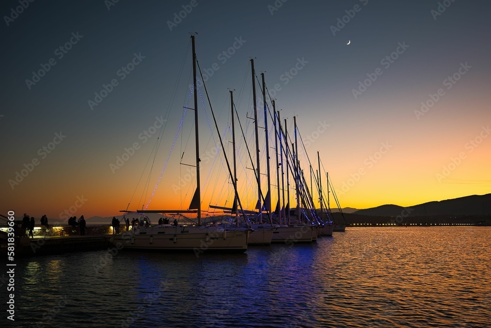 great sunset in the harbor, boats and sailboats tied to the dock, reflections, Volos, Greece