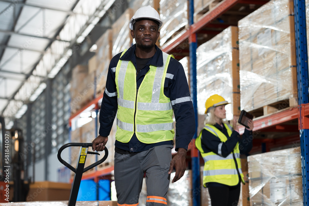African American male warehouse worker pushing load cart in storage warehouse. Male warehouse worker moving boxes of products at distribution branch .Inspection quality control African American male warehouse worker pushing load cart in storage warehouse. Male warehouse worker moving boxes of products at distribution branch .Inspection quality control