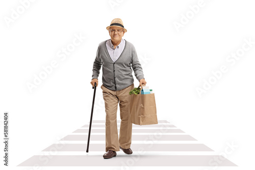 Full length portrait of an elderly man with a cane walking at a pedestrian crossing and carrying a grocery bag