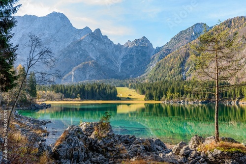 Scenic view of Lake Fusine with shallow water surrounded by trees and rocks against steep mountains