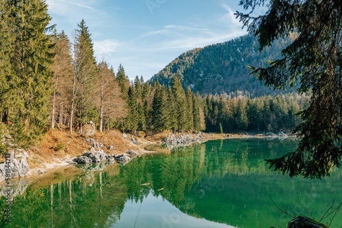 Fototapeta Naklejka Na Ścianę i Meble -  Scenic landscape of Lake Fusine with shallow water surrounded by trees and rocks in Italy