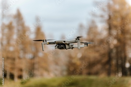 Selective closeup focus of a small drone in the air with an autumn forest view in the background
