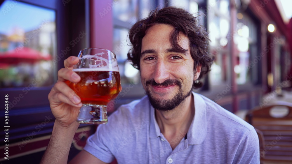 Happy person drinking beer outdoors smiling at camera. Portrait of one young man holding glass of alcohol drink