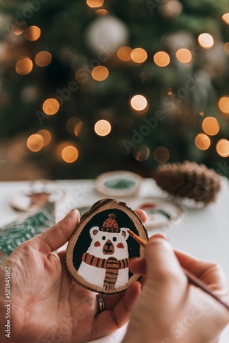 Female hand making diy christmas ornament, painting on a wooden slice