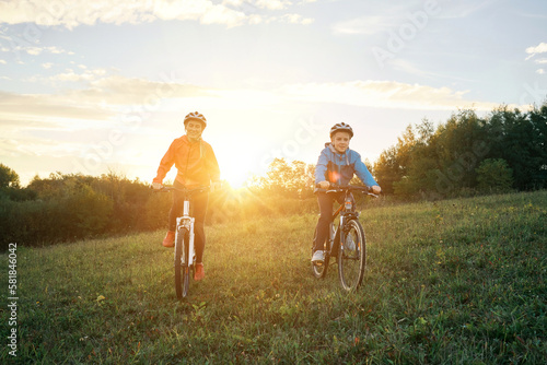 Happy family outdoors, Mother and son ride a bike. Happy cute boy in helmet learn to riding a bike in park on green meadow in autumn day at sunset time. 